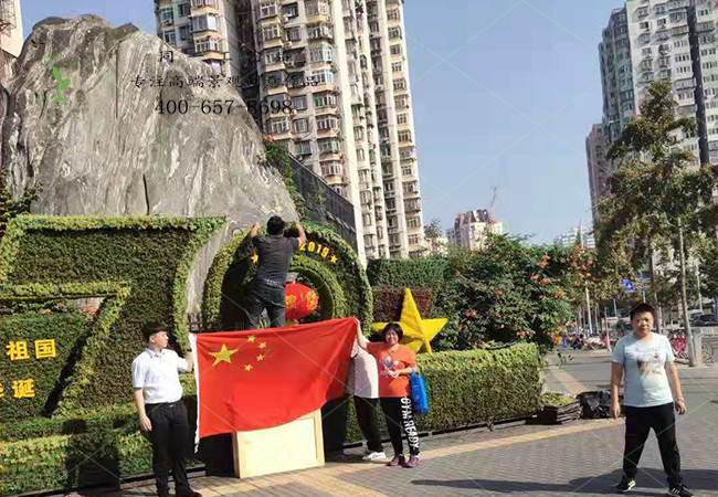 北京游客在植物綠雕國慶綠雕前舉國旗合影